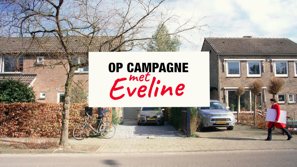 Straat. Eveline komt in rode jas met witte kartonnen onder haar arm aanlopen. Tekst: Op campagne met Eveline