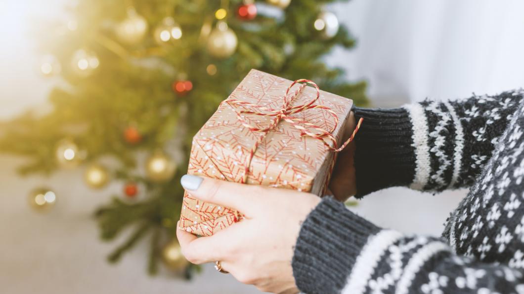 Handen geven een cadeautje. Op de achtergrond staat een kerstboom