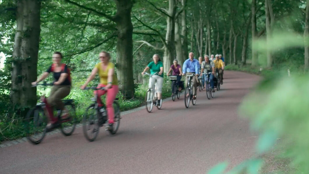 Een rij snelle (onscherpe) fietsers op een breed fietspad door het bos